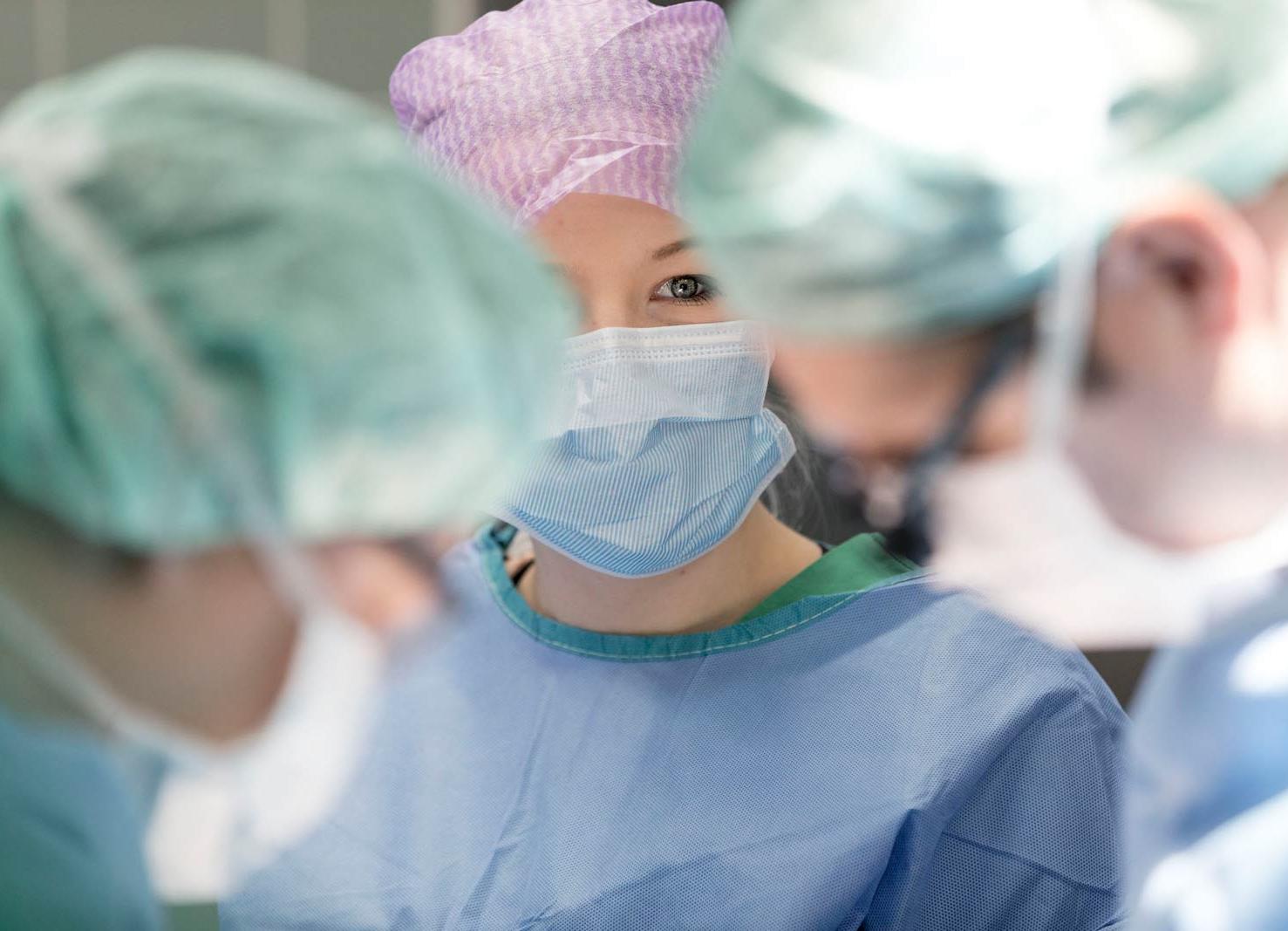 Drei Ärzte in Operationskleidung. Eine Ärztin schaut in die Kamera.
